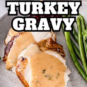 Homemade turkey gravy made with pan drippings drizzled on top of sliced turkey on plate.