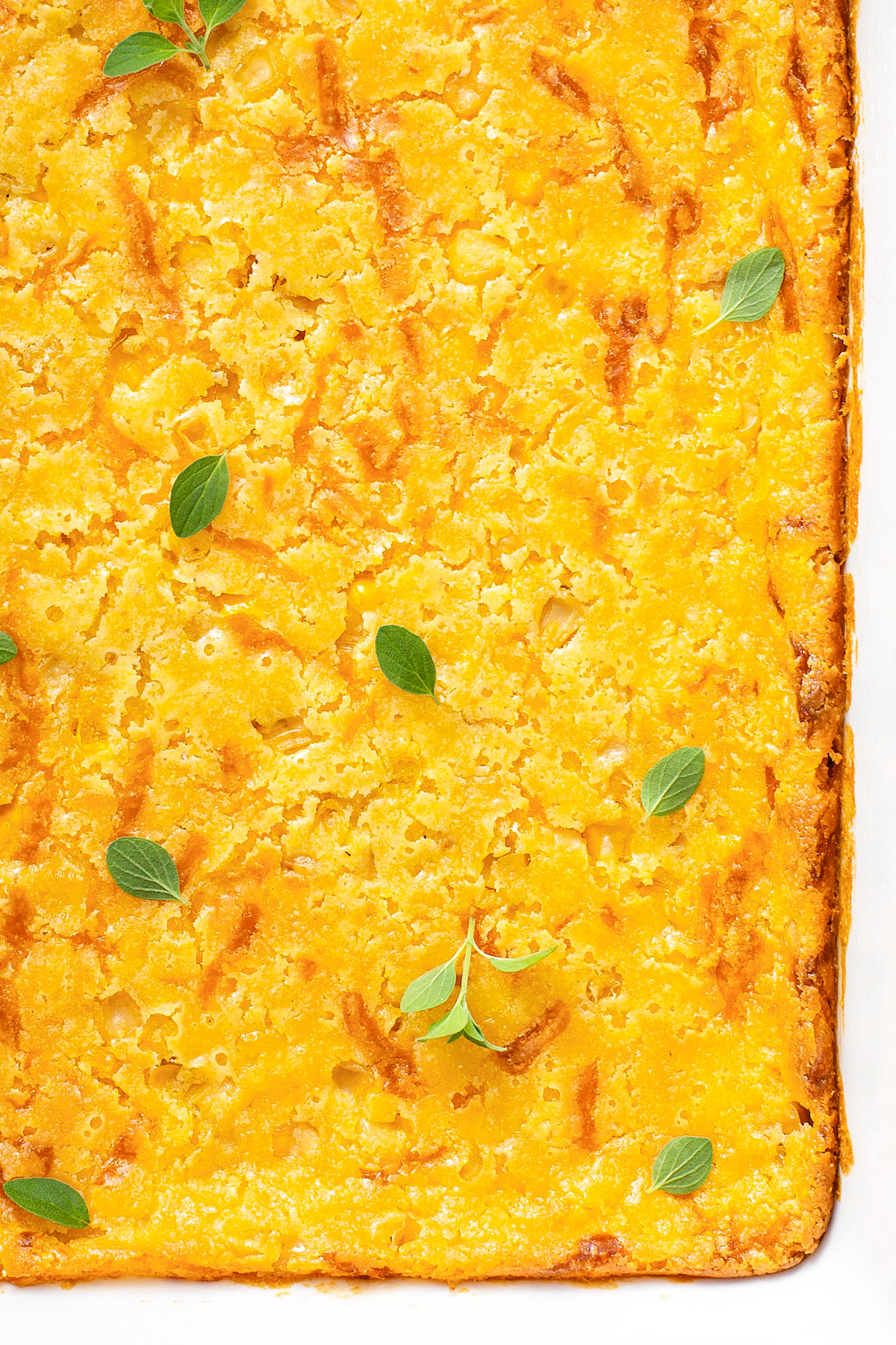 Sweet and cheesy jiffy corn casserole baked in a 9x13 baking dish with fresh herbs sprinkled on top.