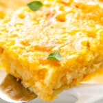 A slice of corn casserole on a spatula being lifted out of a white baking dish.