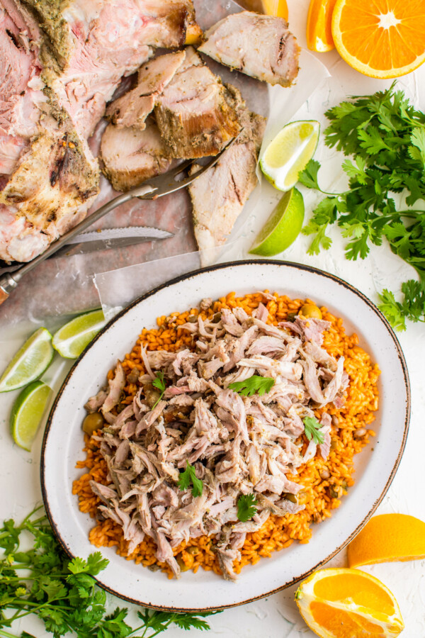 Puerto Rican pernil served over a bed of arroz con gandules with the whole roasted pork shoulder in the background.