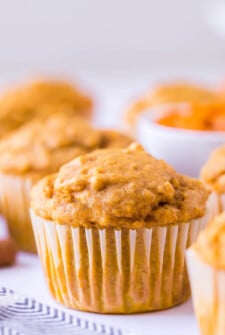 Up close image of a pumpkin oat muffin surrounded by other muffins on a tea towel.