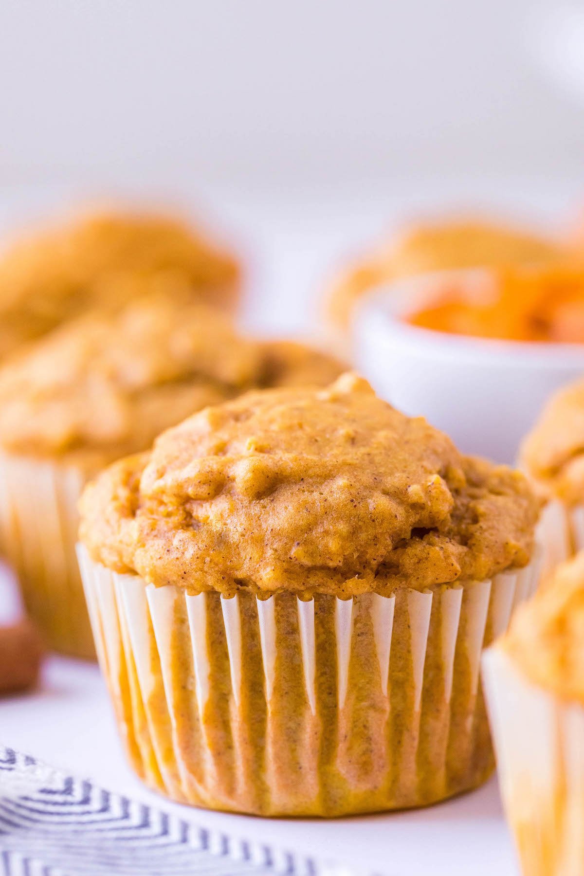 Up close image of a pumpkin oat muffin surrounded by other muffins on a tea towel.