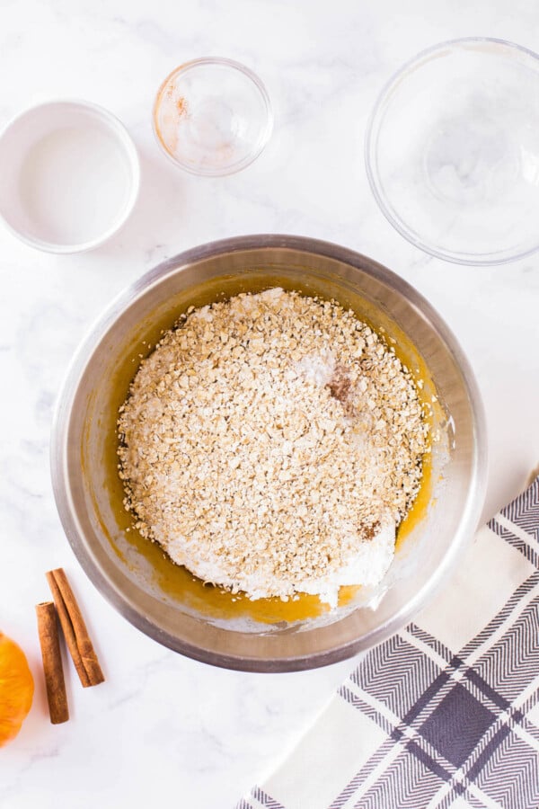 Oats being added into pumpkin muffin batter in a bowl.