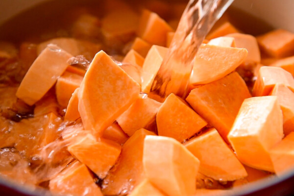 Cubed sweet potatoes in a pot with water being poured over the top.