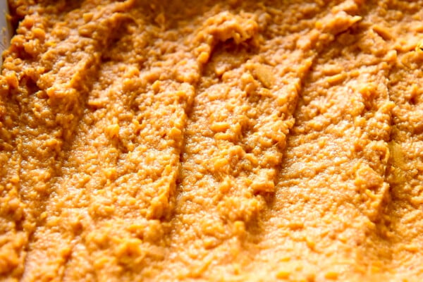 Mashed and seasoned sweet potatoes being spread into an even layer in a casserole dish.