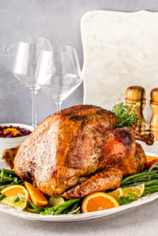 A golden brown roasted turkey over a bed of green beans and citrus on a large serving platter.