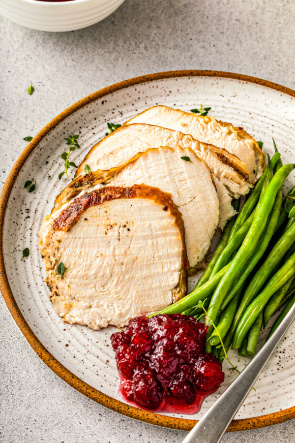 Sliced roasted turkey on a plate with green beans and a scoop of cranberry sauce.