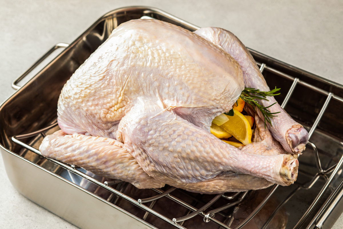 Raw turkey in a roasting pan with aromatics stuffed into the cavity.