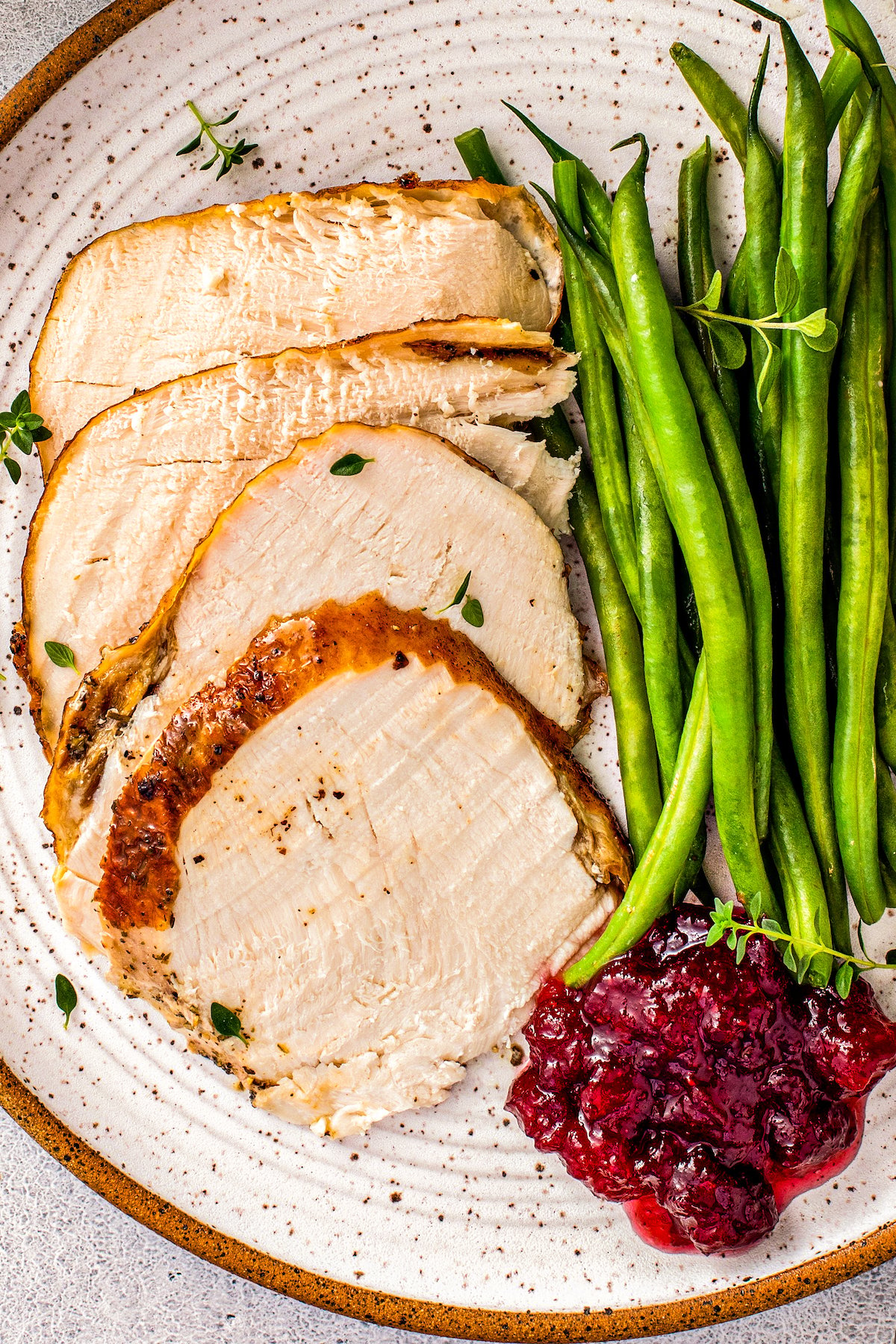 Cooked and sliced brined turkey on a plate with cranberry sauce and green beans.