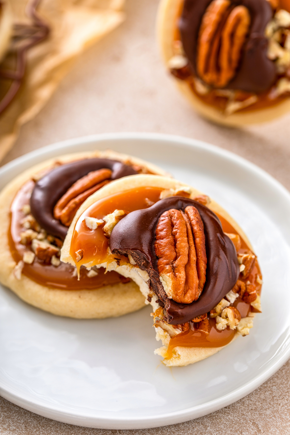 A bite taken out of a soft sugar cookie topped with caramel, pecans and chocolate on a plate.