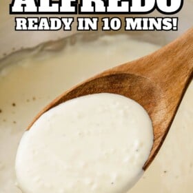 Alfredo sauce in a wooden spoon being scooped out of a skillet.