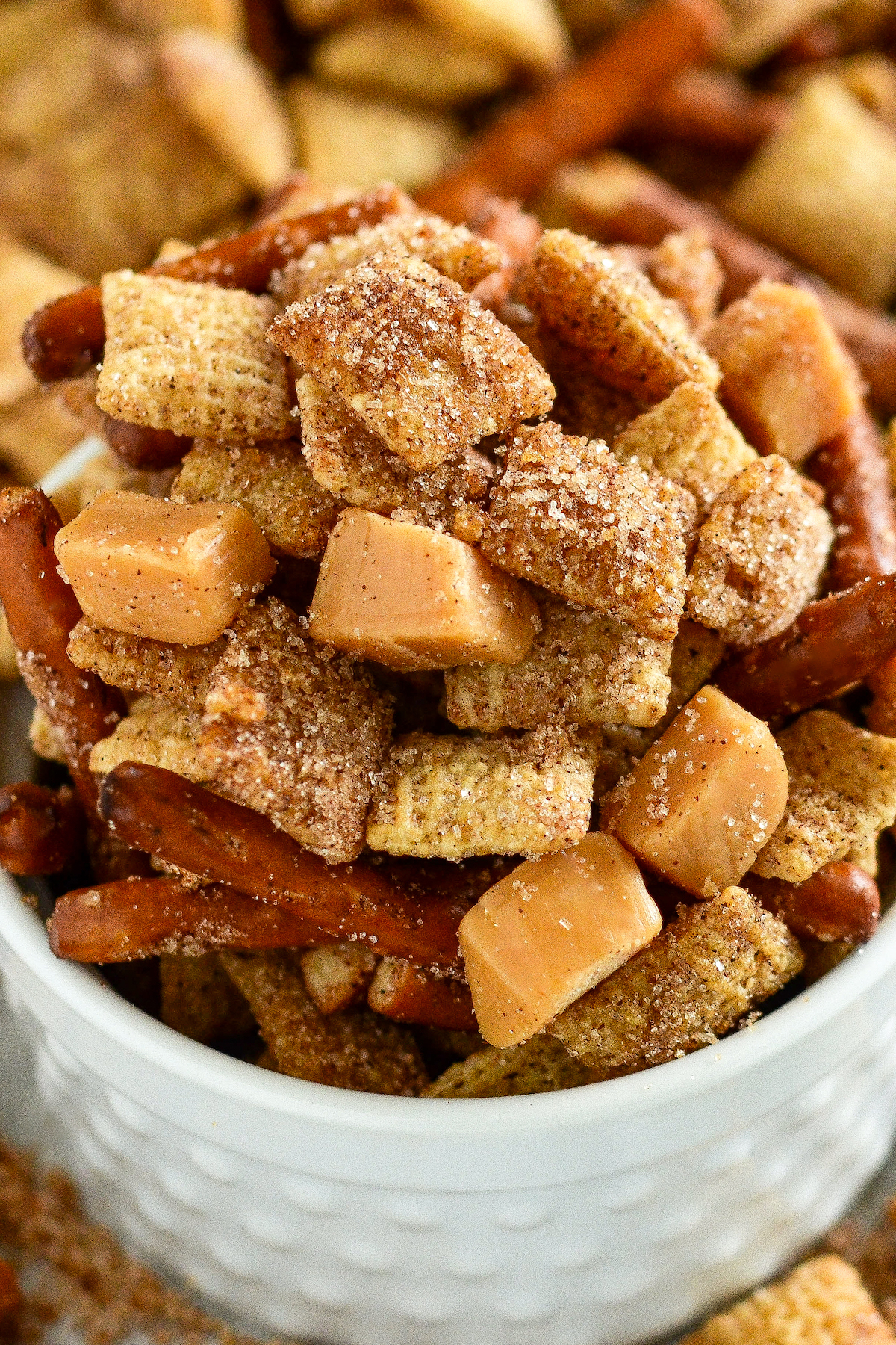 A bowl of churro Chex mix with pretzels and caramel squares.