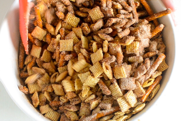 Cinnamon sugar poured on top of Chex mix and being tossed to coat in the mixture.