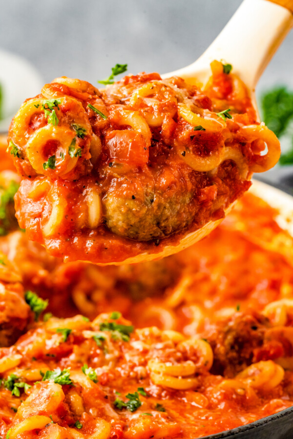 Spoonful of homemade spaghettios and meatballs in their tomatoey sauce being lifted out of a skillet.