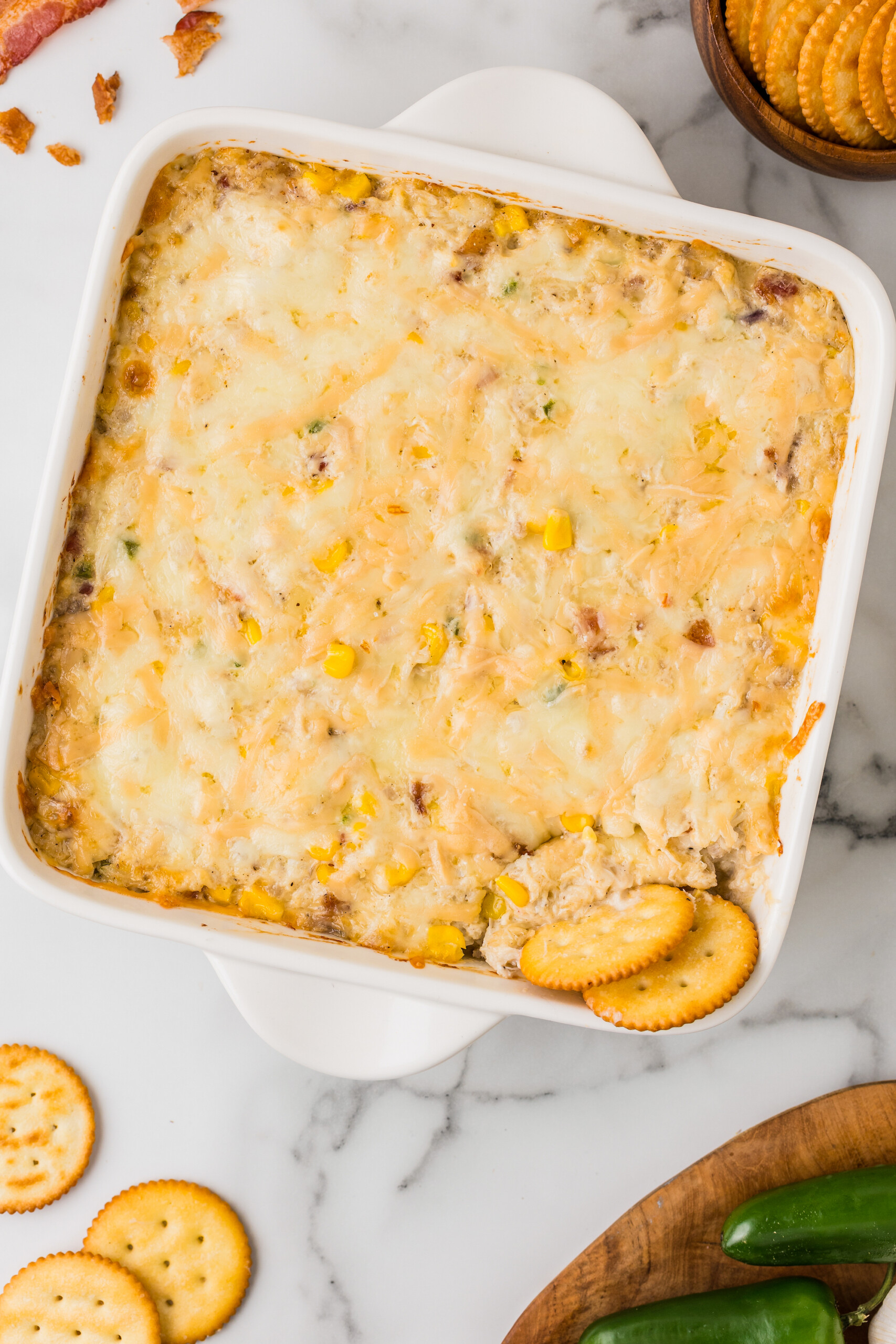 Creamy hot crab dip baked in casserole dish with crackers scooping out a bite.