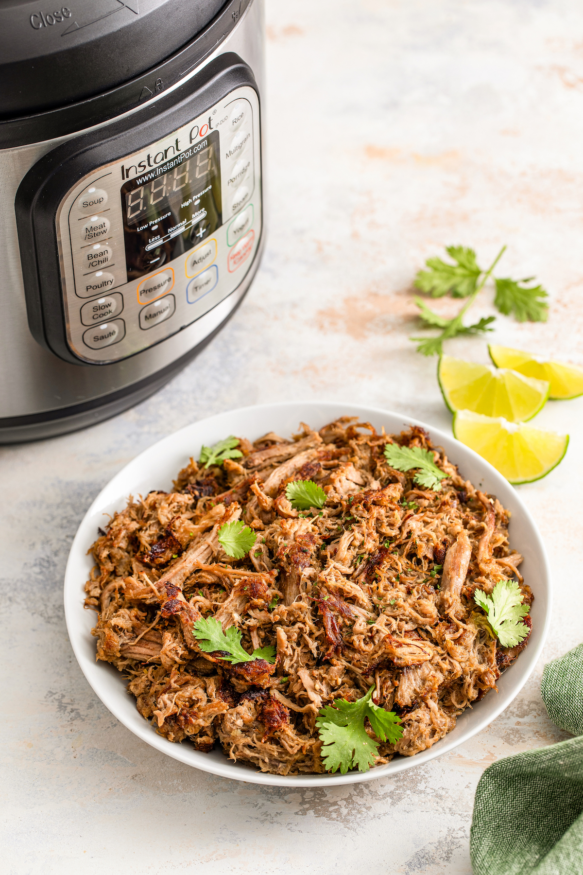 Bowl of Instant Pot carnitas with an Instant Pot in the background. 