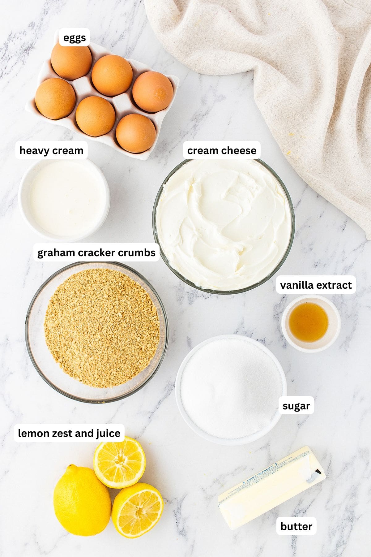 The ingredients for lemon cheesecake recipe in order from top to bottom: eggs, heavy cream, cream cheese, graham cracker crumbs, sugar, vanilla extract, sugar, lemons and butter. 