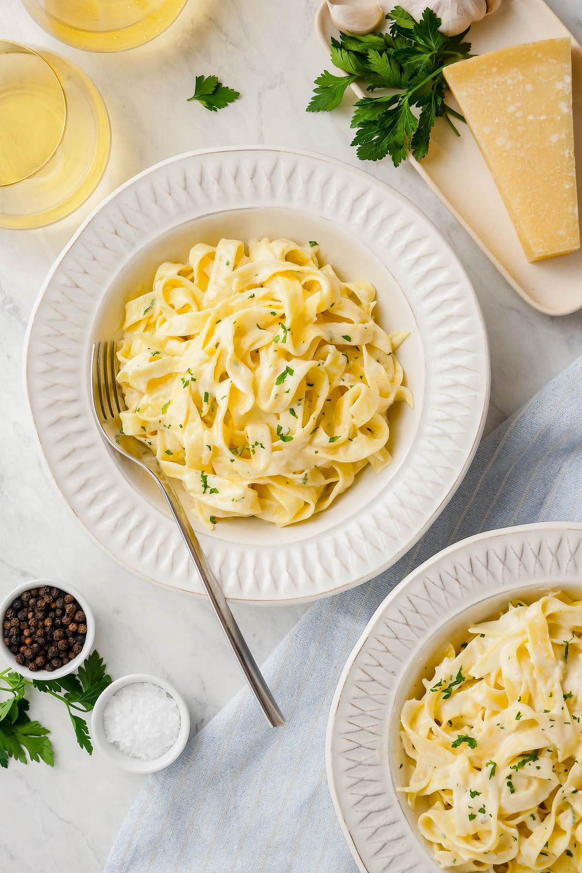 An overhead view of fettuccine coated in sauce served on plates with fresh parsley sprinkled on top.