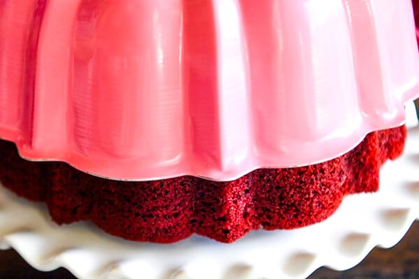 Bundt cake pan being lifted off the red velvet cake on a cake stand.