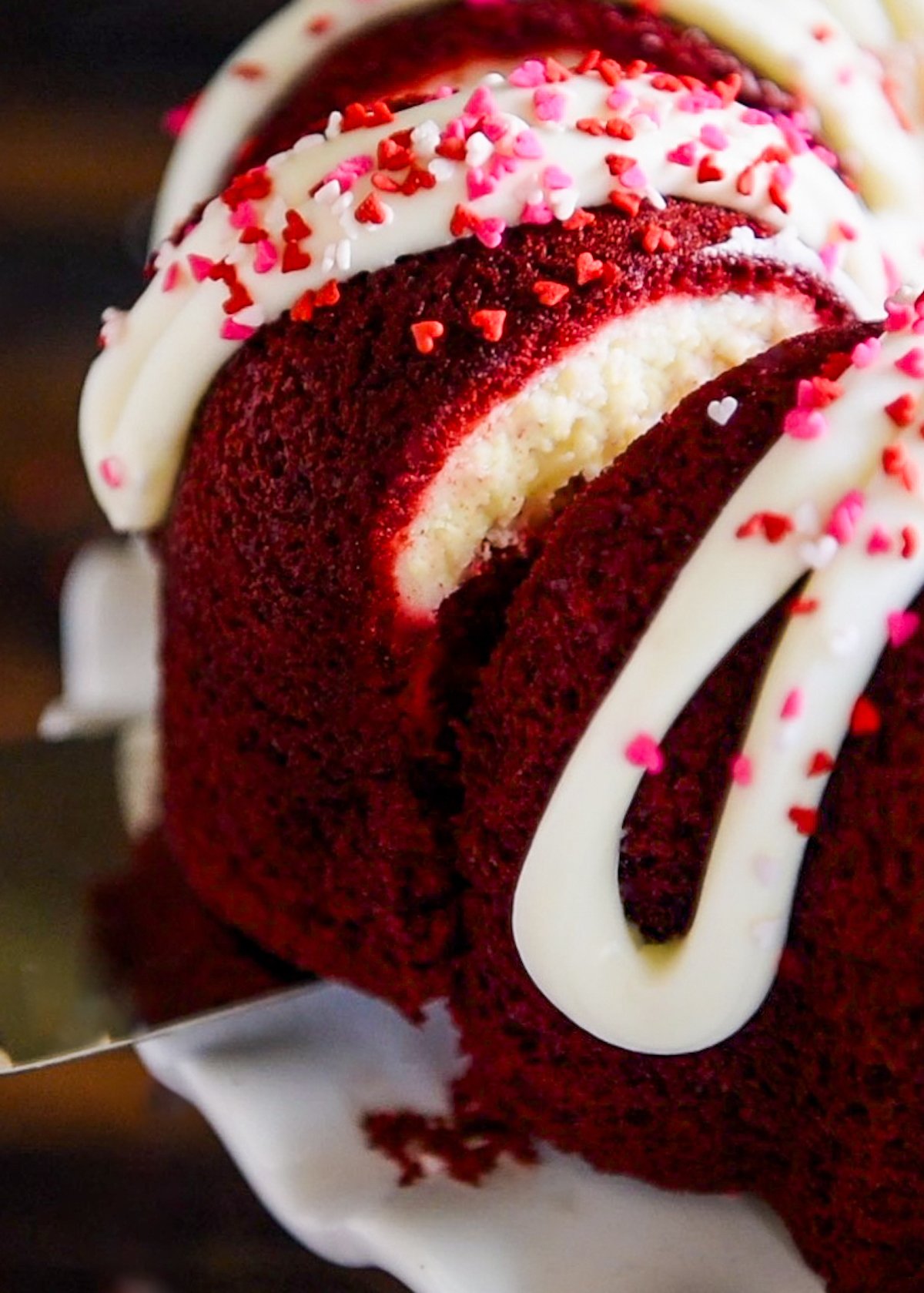 A slice of red velvet cream cheese bundt cake being lifted with a serving spatula from the cake.