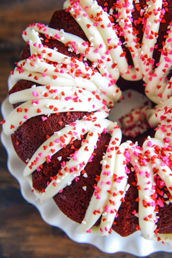 Overhead image of a red velvet bundt cake drizzled with cream cheese icing on top with sprinkles on top.