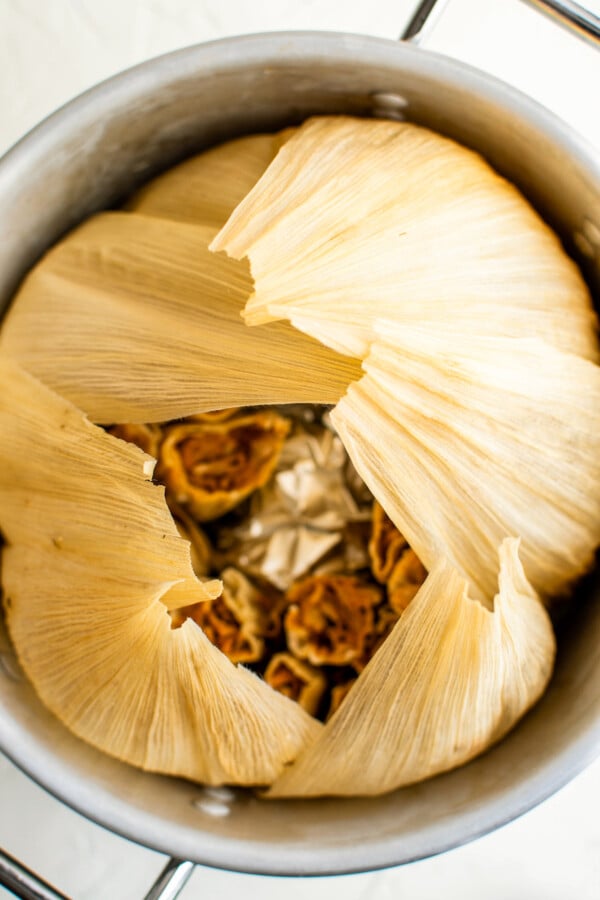 Tamales in a large pot with corn husks wrapped over the top to trap the steam.