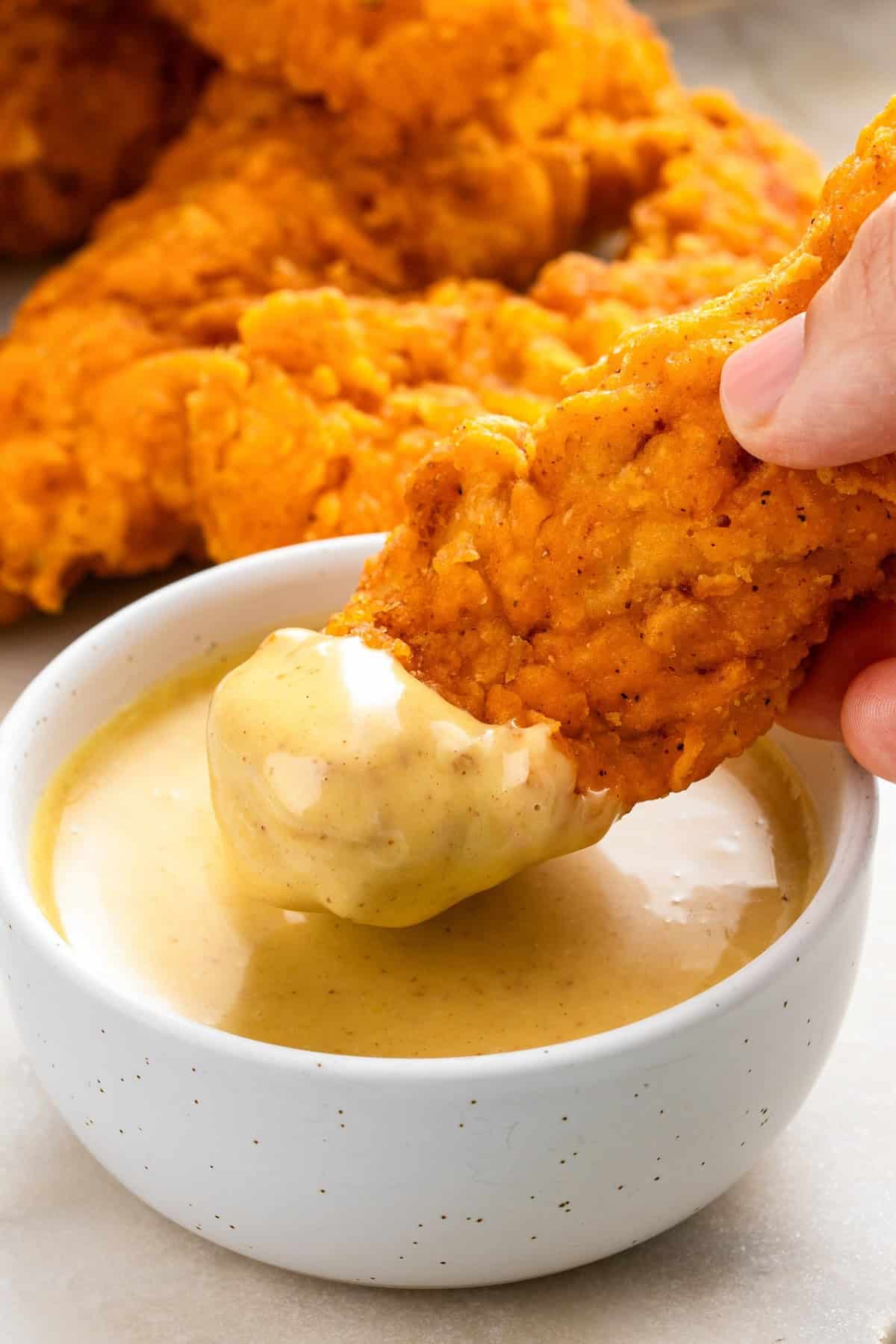 A chicken tender is being dipped into honey mustard sauce.