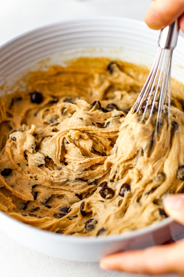 Cookie dough loaded with chocolate chips being mixed together with a whisk.