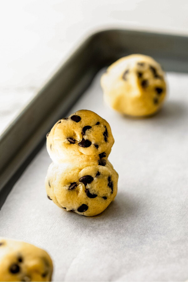 Cookie dough balls stacked on top of each other on a baking sheet.