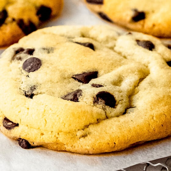 A thick and chewy chocolate chip cookie resting on a cooling rack lined with parchment paper.