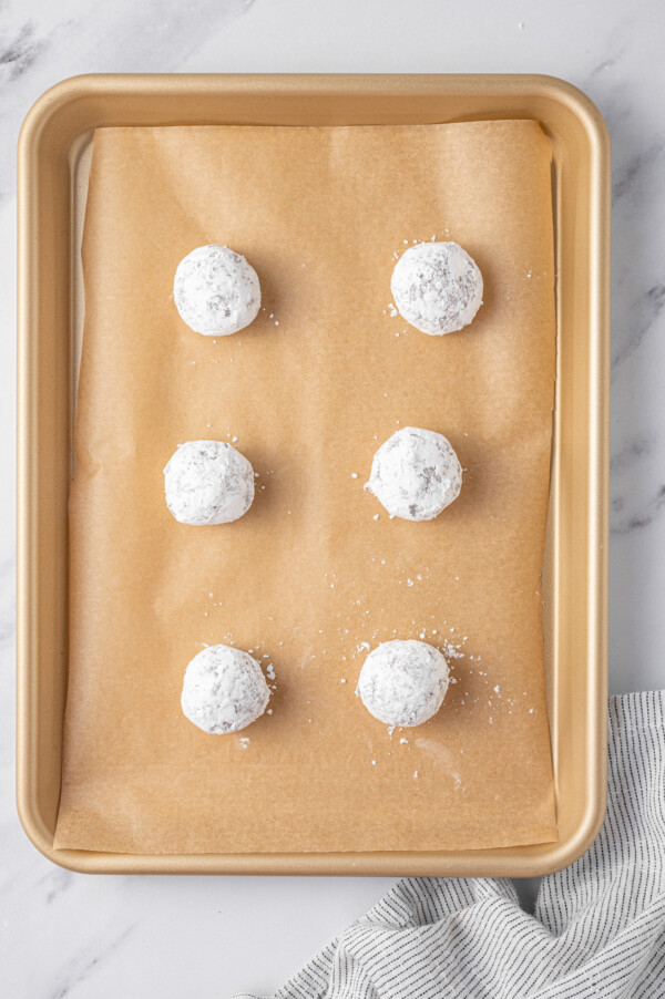 Chocolate cookie dough balls coated in powdered sugar on a baking sheet lined with parchment paper.