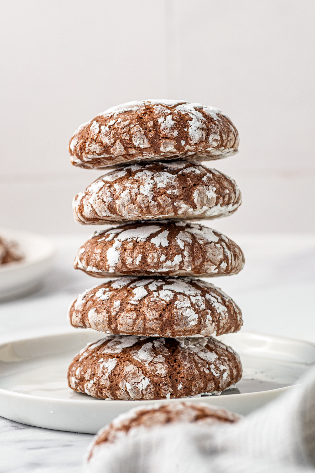 Five chocolate crinkle cookies stacked on top of each other on a plate.