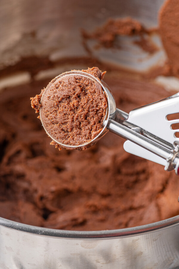 A cookie scoop scooping out a ball of chocolate cookie dough from a mixing bowl of dough.