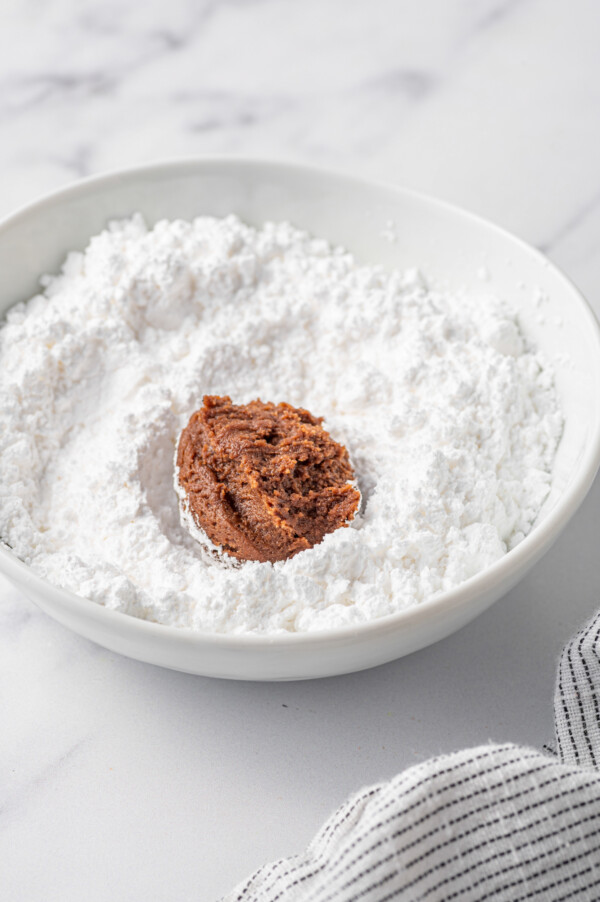 A ball of chocolate cookie dough in a bowl of powdered sugar.