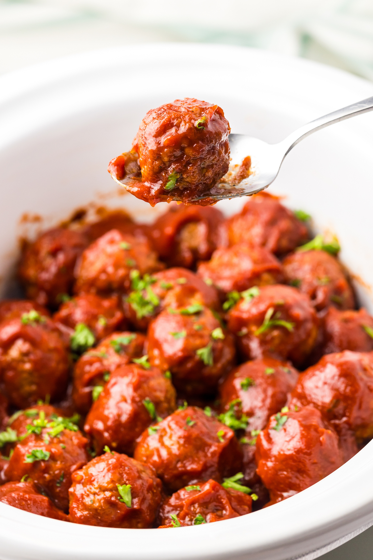 Barbecue meatballs in a crockpot with a spoon scooping out a meatball coated in bbq sauce.
