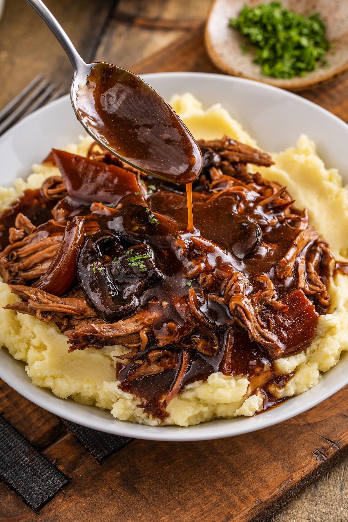A spoon drizzling brown gravy over a serving of crockpot pot roast.
