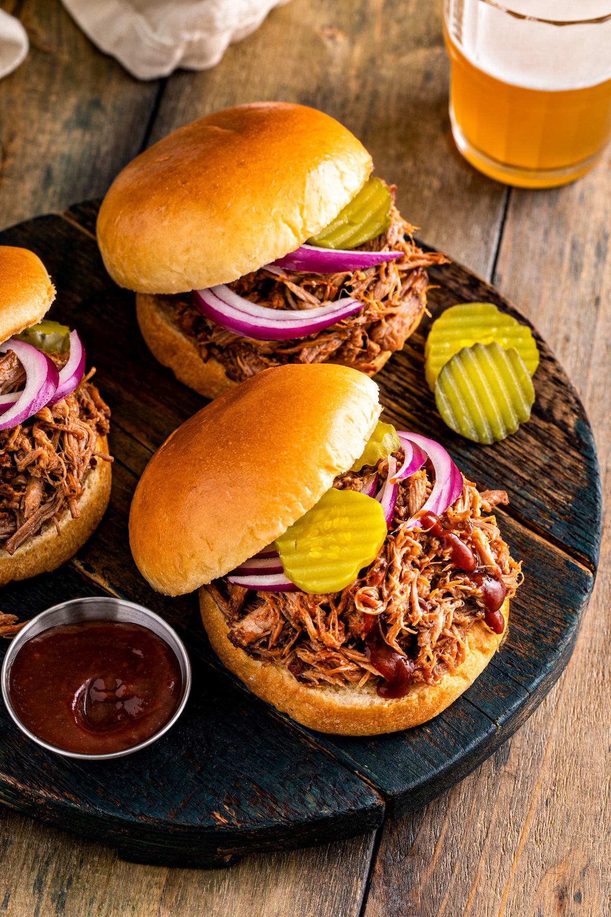Three pulled pork sandwiches with a side of bbq sauce and a beer.