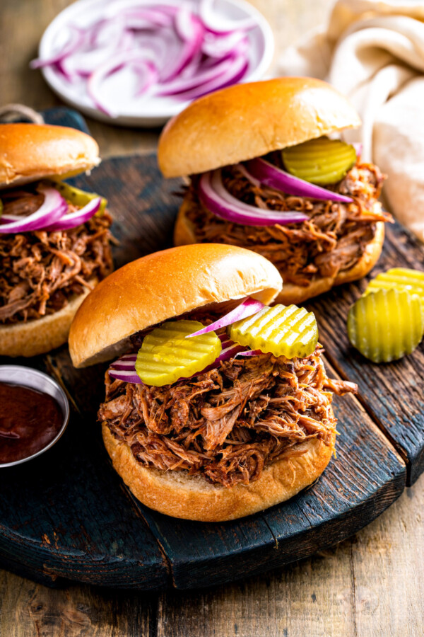 Three crockpot pulled pork sandwiches topped with pickles and sliced red onions.