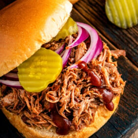 A slow cooker pulled pork sandwich topped with red onions, pickles and a drizzle of bbq sauce.