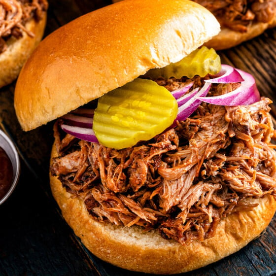 A crockpot pulled pork sandwich on a tray with sliced red onions and pickles on top.