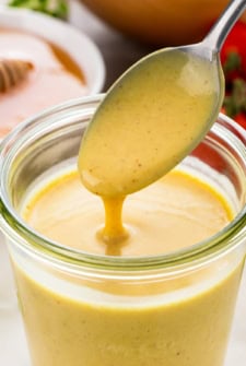 Homemade honey mustard dipping sauce is being drizzled into a jar with a spoon.