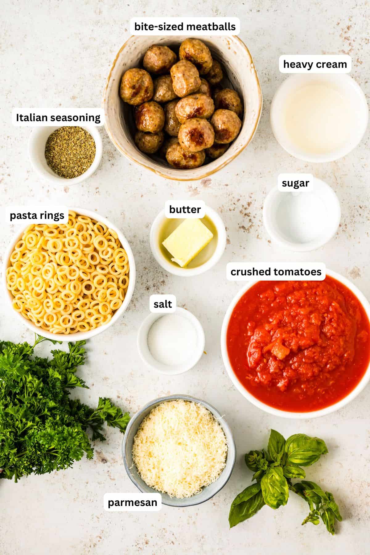 The ingredients for spaghettios recipe in order from top to bottom: frozen mini meatballs, italian seasoning, butter, heavy cream, sugar, pasta rings, salt, crushed tomatoes, parmesan.