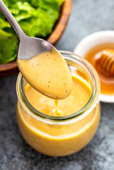 A spoon spooning homemade honey mustard sauce into a glass jar.