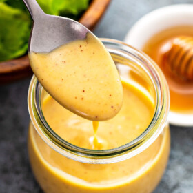 A spoon spooning homemade honey mustard sauce into a glass jar.