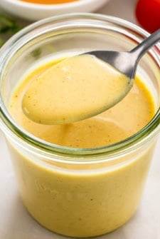 A spoon is lifting some sweet and tangy dipping sauce out of a jar.