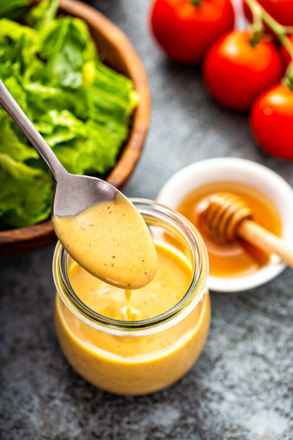 A spoon drizzling homemade honey mustard sauce into a glass jar.