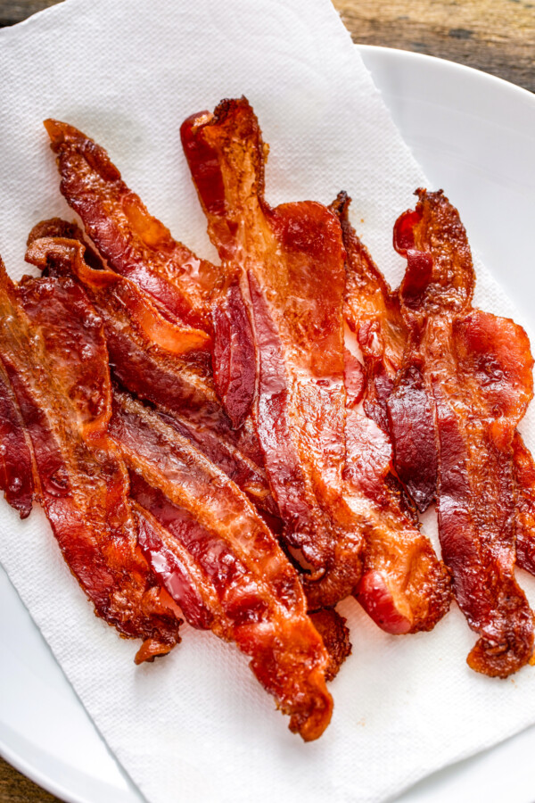 Crispy oven baked bacon arranged on a plate lined with a paper towel to soak up any excess grease.