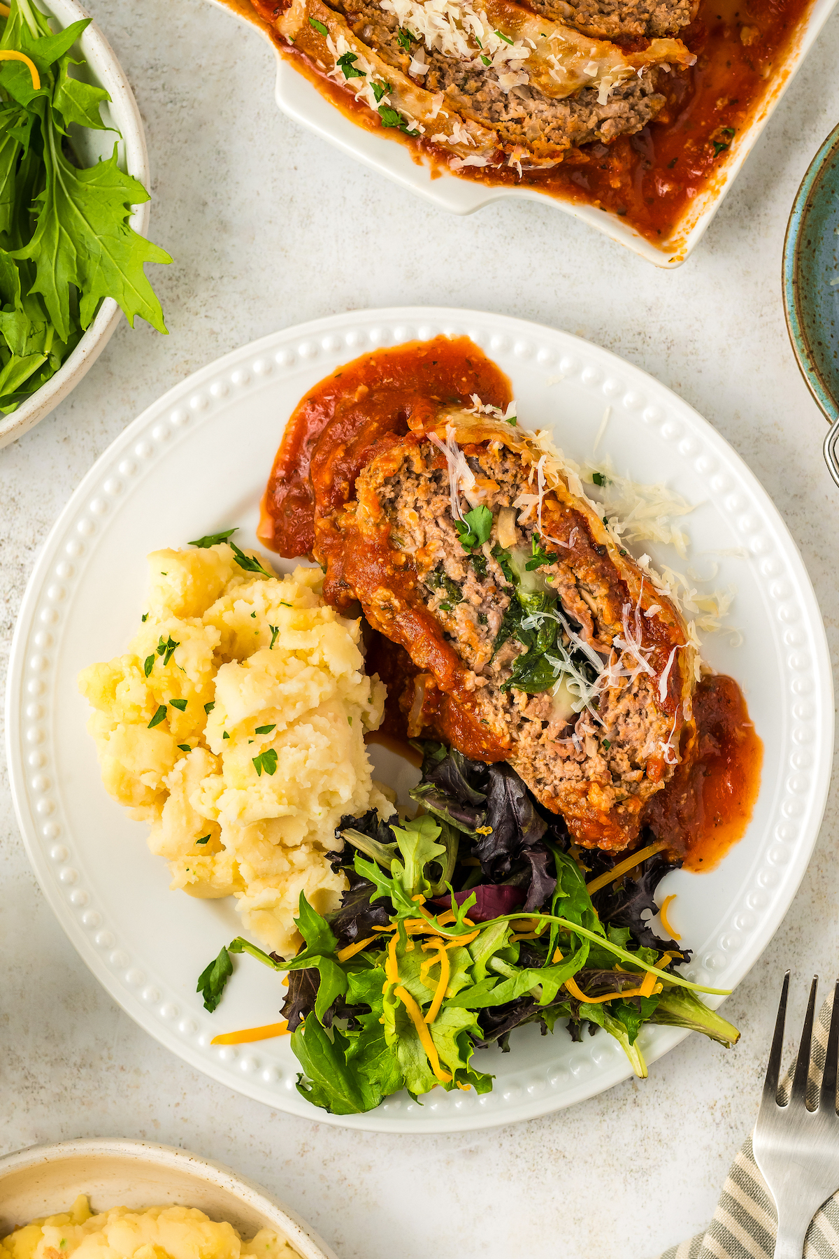 Italian meatloaf on a plate with a side of green salad and mashed potatoes.