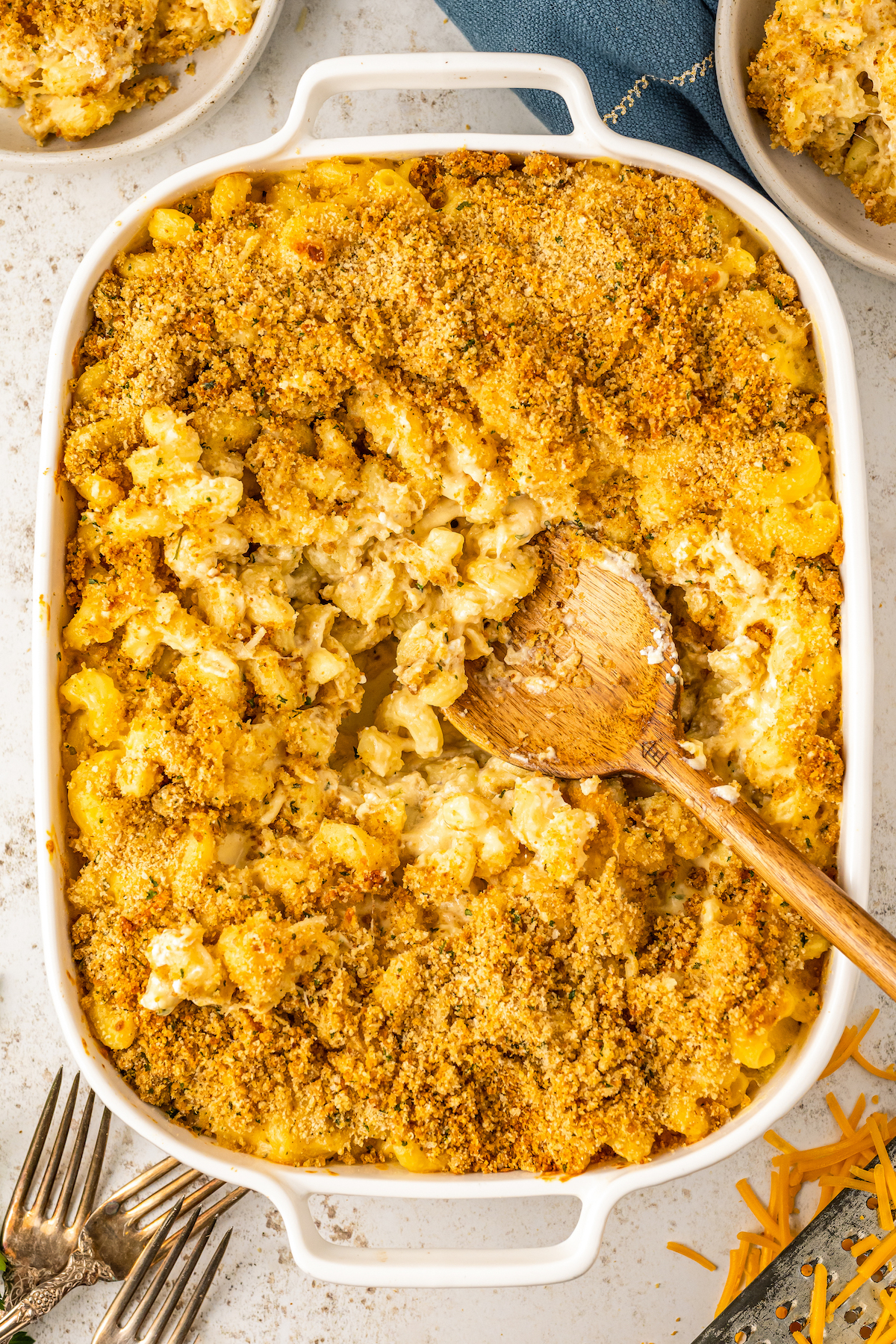 Extra cheese and creamy mac and cheese in a casserole dish after baking with a crispy panko breadcrumb topping and a wooden spoon in the casserole ready to serve.