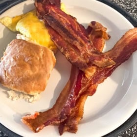 Crispy bacon is plated with a biscuit and cheesy eggs.